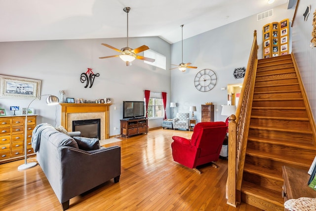 living area with visible vents, light wood-style flooring, a fireplace with flush hearth, stairway, and high vaulted ceiling