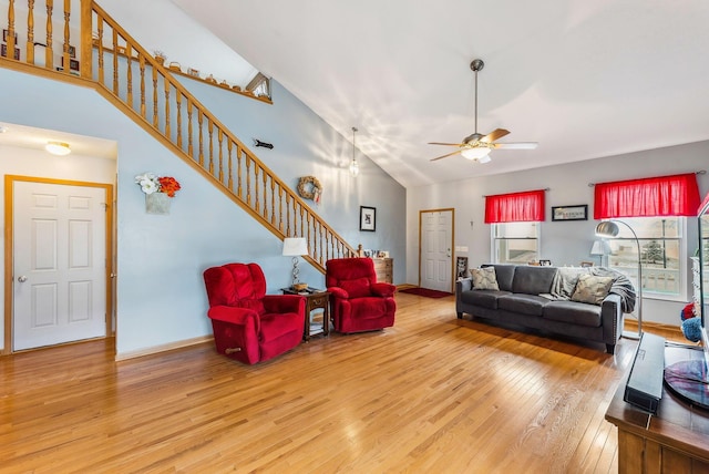 living area featuring baseboards, a ceiling fan, hardwood / wood-style flooring, stairs, and high vaulted ceiling