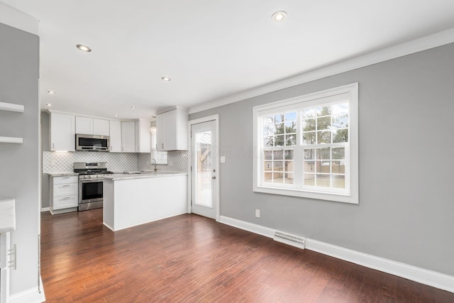 kitchen featuring white cabinets, dark wood-style floors, stainless steel appliances, light countertops, and backsplash