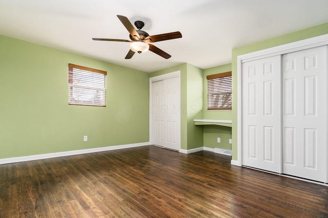 unfurnished bedroom featuring dark wood-style flooring, visible vents, baseboards, and two closets