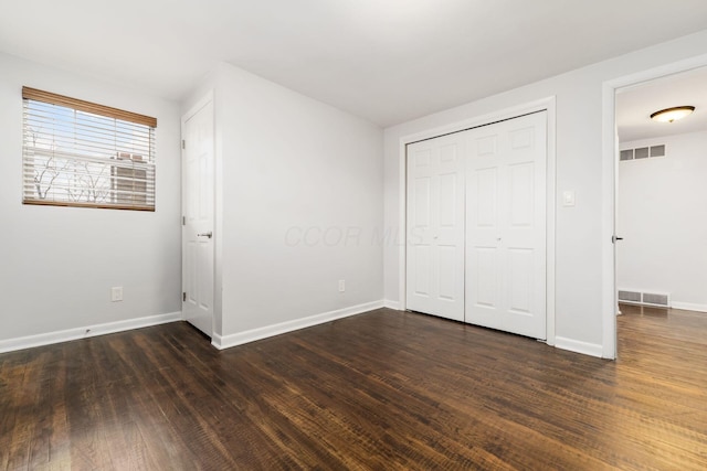 unfurnished bedroom with dark wood-style flooring, visible vents, and baseboards