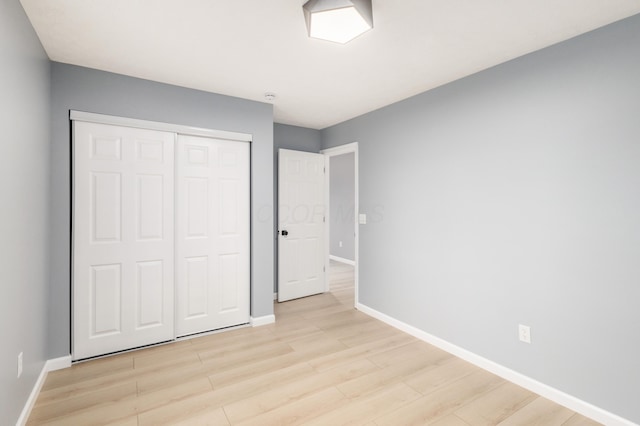 unfurnished bedroom featuring light wood-style flooring, baseboards, and a closet