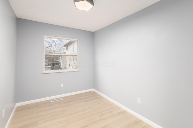 empty room with wood finished floors, visible vents, and baseboards