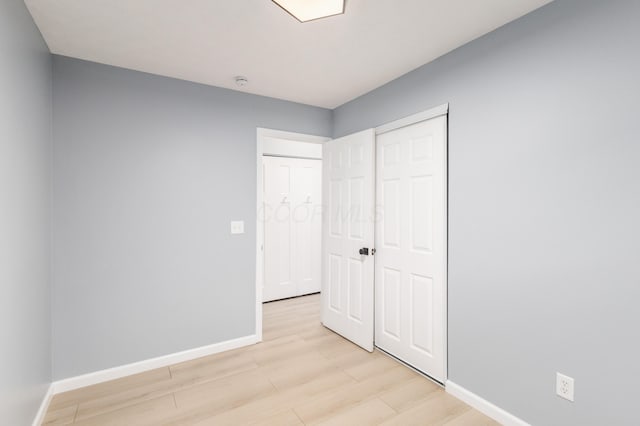 unfurnished bedroom with light wood-type flooring, a closet, and baseboards