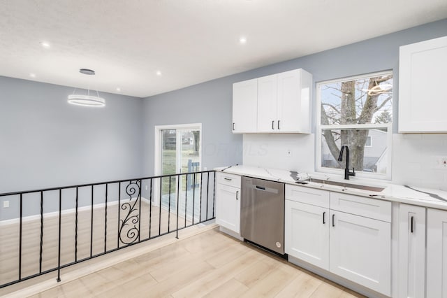 kitchen featuring light stone counters, stainless steel dishwasher, white cabinets, a sink, and plenty of natural light