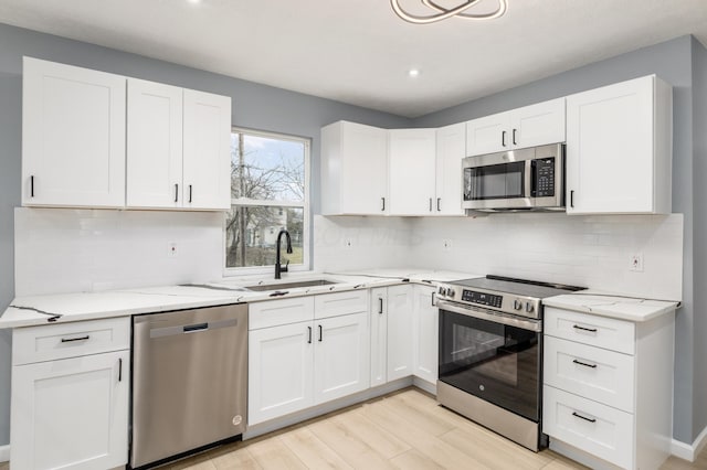 kitchen with light stone counters, stainless steel appliances, light wood-style floors, white cabinetry, and a sink