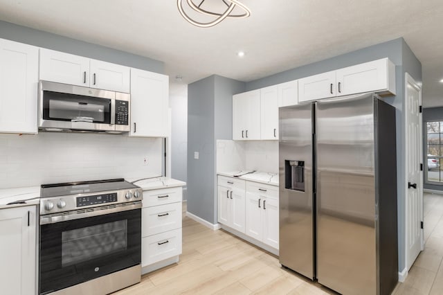 kitchen with light wood finished floors, tasteful backsplash, appliances with stainless steel finishes, light stone countertops, and white cabinetry