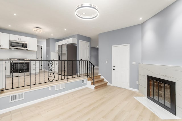 interior space featuring a fireplace, visible vents, stairway, light wood-style flooring, and baseboards