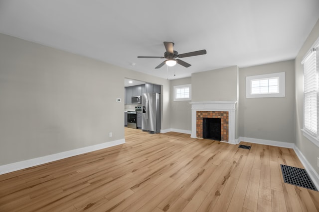 unfurnished living room with a brick fireplace, visible vents, light wood-style flooring, and baseboards