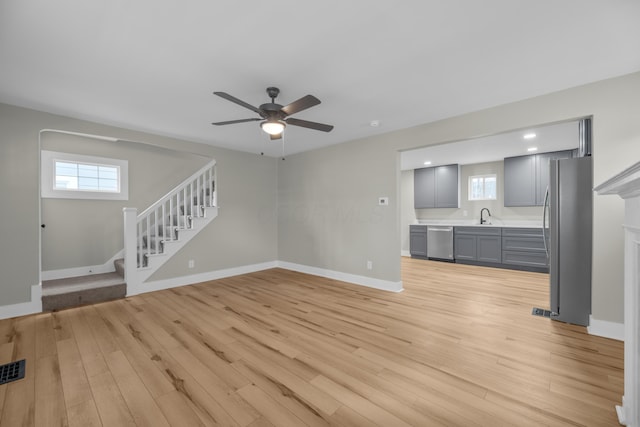 unfurnished living room featuring light wood-style floors, a ceiling fan, a sink, baseboards, and stairs