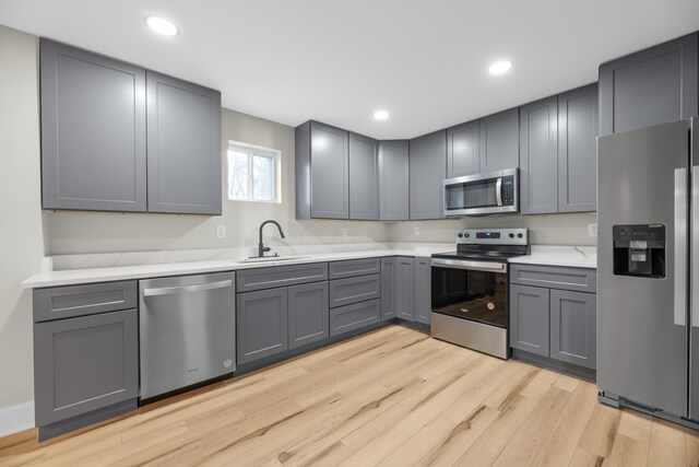 kitchen featuring light wood finished floors, gray cabinets, light countertops, appliances with stainless steel finishes, and a sink