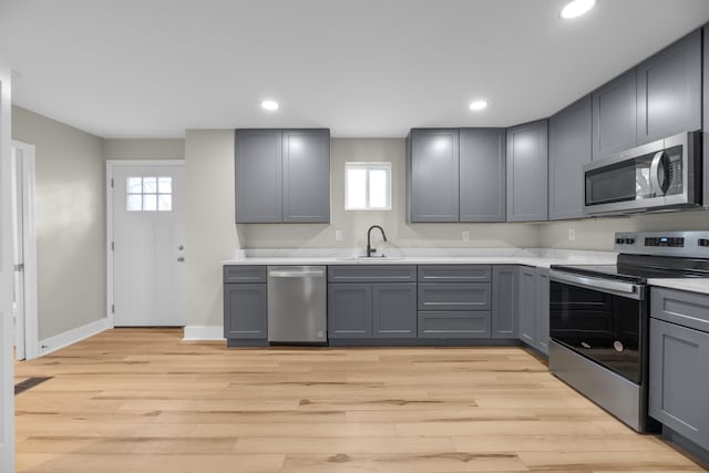 kitchen featuring appliances with stainless steel finishes, light countertops, light wood-style floors, and gray cabinetry