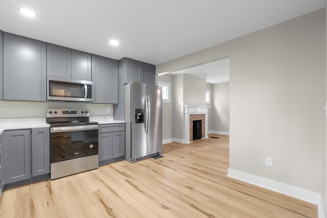 kitchen with baseboards, light wood-style flooring, appliances with stainless steel finishes, gray cabinetry, and a brick fireplace