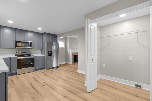 kitchen featuring light wood-type flooring, stainless steel appliances, light countertops, and gray cabinetry