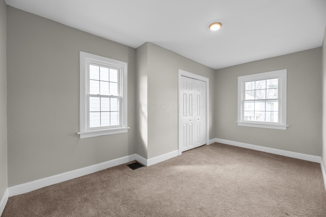 unfurnished bedroom featuring carpet floors, multiple windows, visible vents, and baseboards