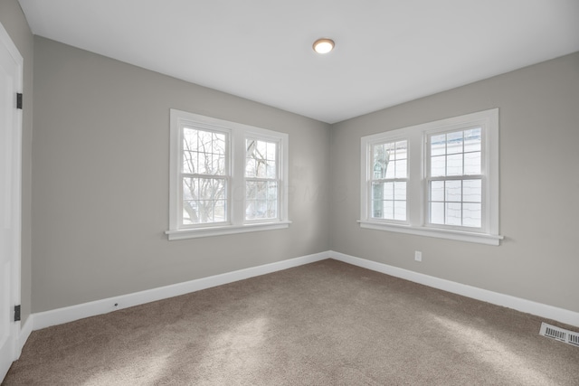 carpeted spare room featuring plenty of natural light, visible vents, and baseboards