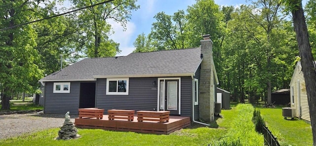 rear view of house featuring roof with shingles, a lawn, and a wooden deck