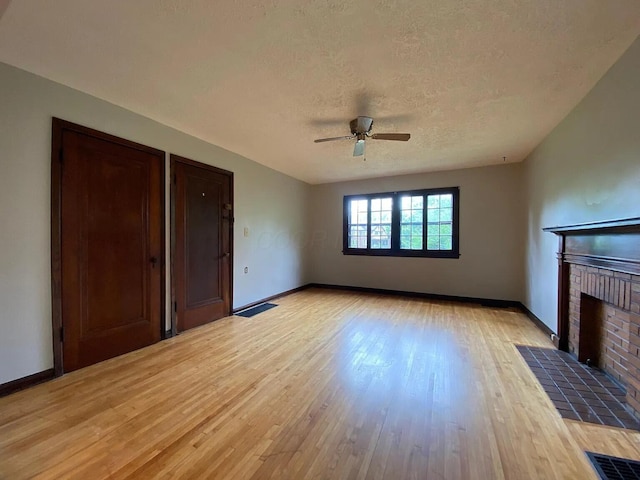 unfurnished living room with visible vents, baseboards, light wood-type flooring, a fireplace, and a textured ceiling