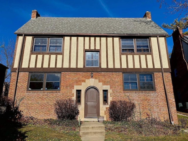 tudor house featuring stucco siding, brick siding, a chimney, and a shingled roof