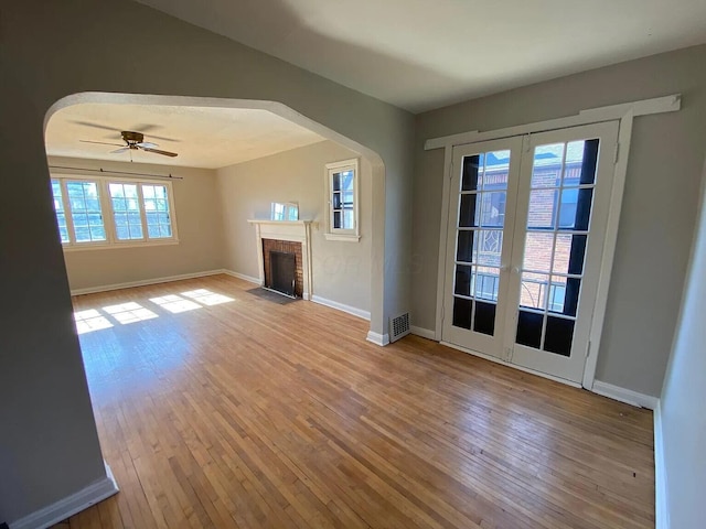 unfurnished living room featuring visible vents, arched walkways, a fireplace, and hardwood / wood-style flooring