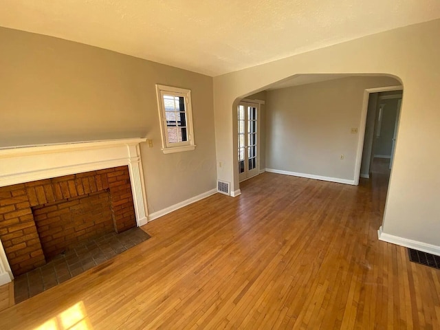 unfurnished living room featuring visible vents, baseboards, a fireplace, arched walkways, and hardwood / wood-style flooring