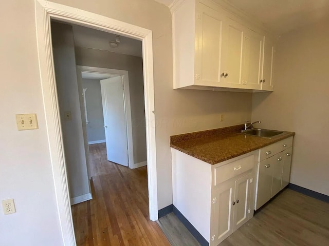 kitchen with dark countertops, white cabinets, wood finished floors, and a sink