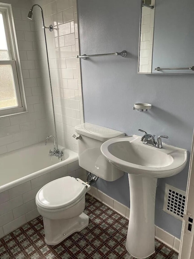 bathroom with tile patterned flooring, toilet, tiled shower / bath, and baseboards