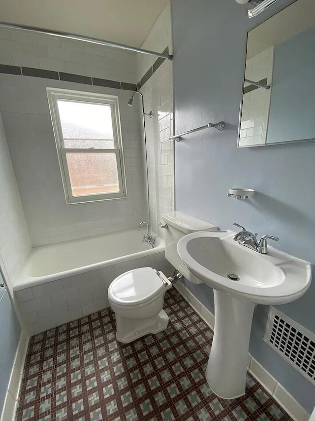 bathroom with tiled shower / bath, baseboards, and toilet