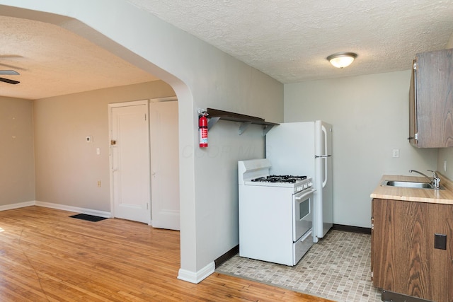 kitchen with light wood finished floors, white range with gas stovetop, arched walkways, ceiling fan, and a sink