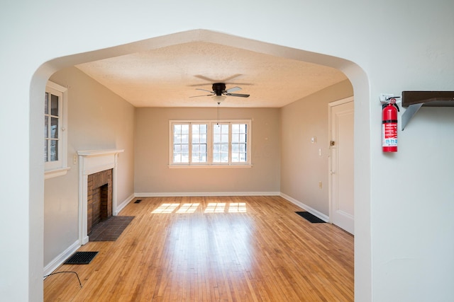 unfurnished living room featuring a ceiling fan, visible vents, arched walkways, light wood-style floors, and a textured ceiling