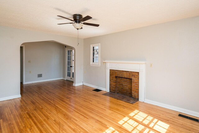 unfurnished living room with light wood-type flooring, visible vents, and arched walkways