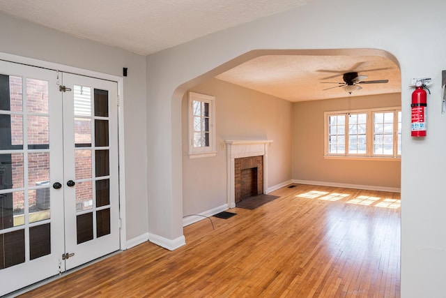 unfurnished living room featuring visible vents, a fireplace with flush hearth, hardwood / wood-style flooring, arched walkways, and a textured ceiling