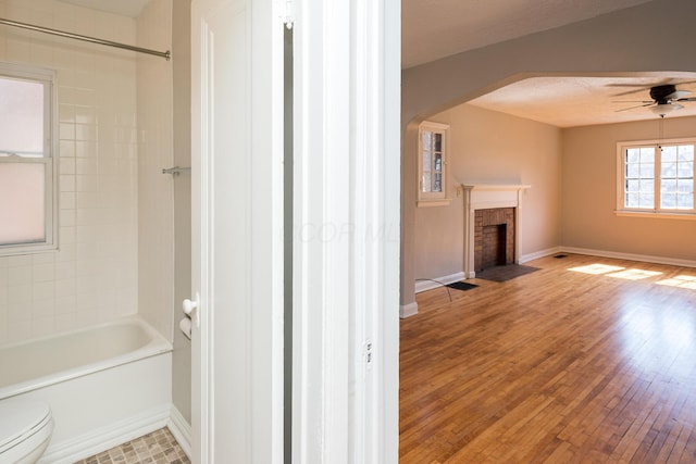 full bathroom with a fireplace with flush hearth, toilet, baseboards, and wood finished floors