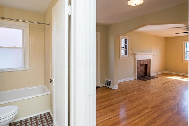 bathroom featuring a ceiling fan, wood finished floors, toilet, and a fireplace