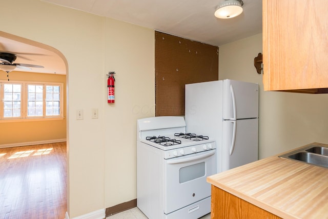 kitchen featuring baseboards, light countertops, arched walkways, white appliances, and a ceiling fan