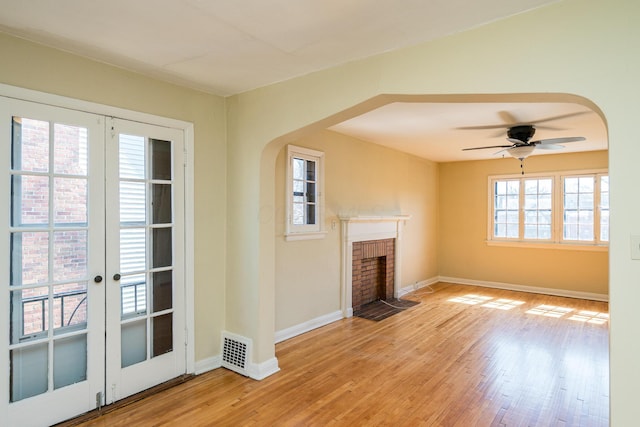 unfurnished living room featuring a brick fireplace, light wood-style floors, baseboards, and arched walkways