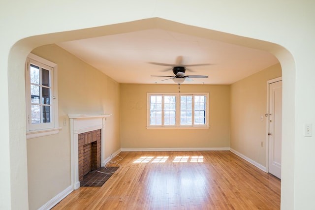 unfurnished living room with light wood finished floors, arched walkways, a fireplace, and baseboards