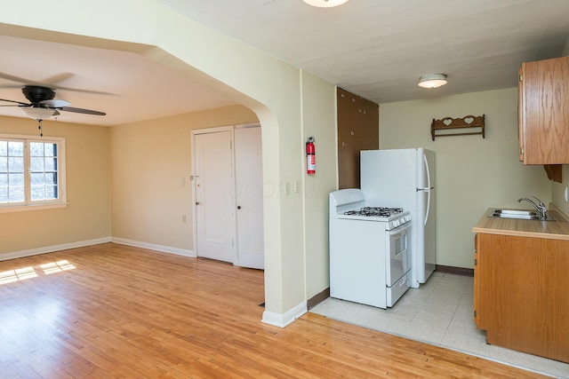 kitchen with white appliances, arched walkways, a sink, light countertops, and light wood-style floors