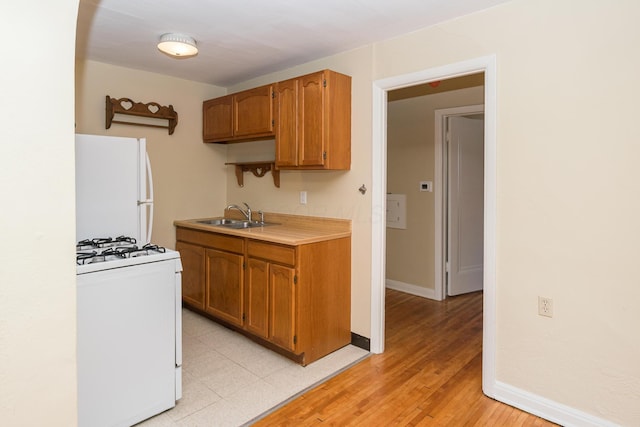 kitchen with white appliances, light countertops, baseboards, and a sink