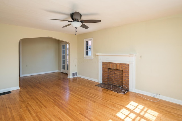 unfurnished living room featuring arched walkways, visible vents, and light wood-style flooring