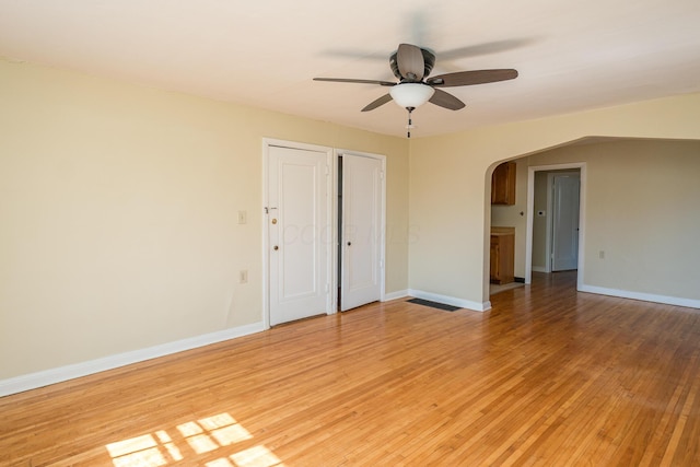 unfurnished bedroom with baseboards, arched walkways, and light wood-style floors