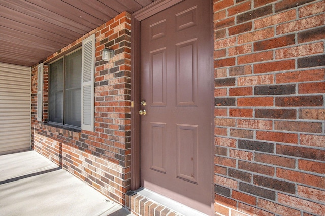 doorway to property featuring a porch and brick siding