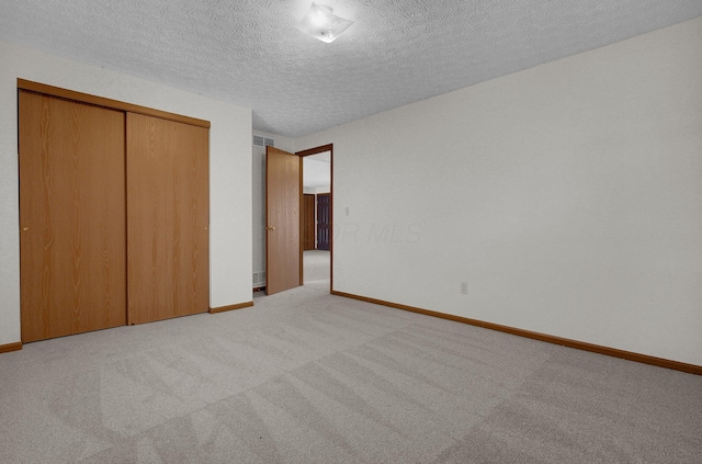 unfurnished bedroom with a textured ceiling, baseboards, a closet, and light carpet