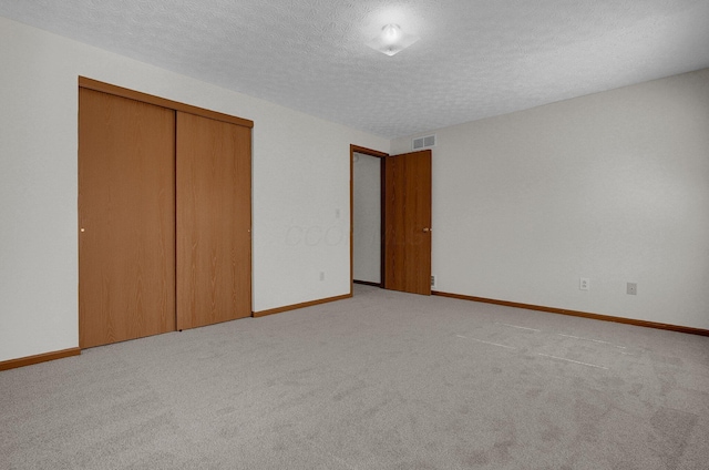 unfurnished bedroom featuring visible vents, baseboards, light colored carpet, a closet, and a textured ceiling