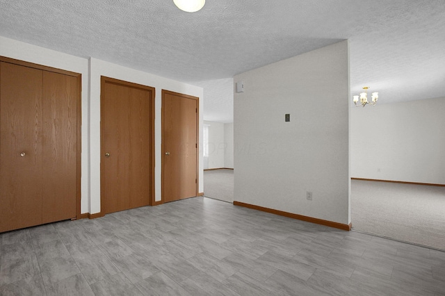 unfurnished bedroom with an inviting chandelier, baseboards, multiple closets, and a textured ceiling