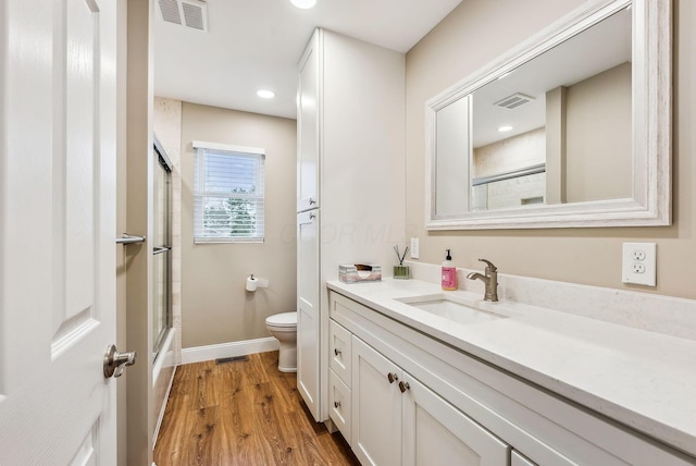 bathroom featuring visible vents, toilet, a shower with door, wood finished floors, and vanity