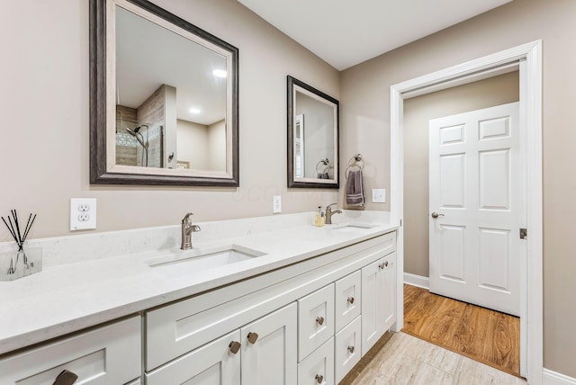 full bathroom featuring wood finished floors, a sink, baseboards, and double vanity