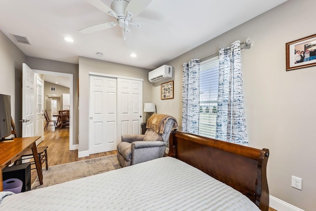 bedroom featuring a wall mounted air conditioner, visible vents, baseboards, and wood finished floors