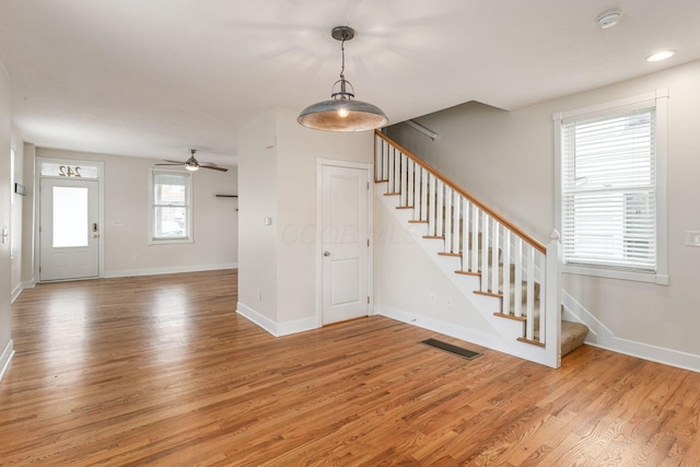 entryway with visible vents, stairway, light wood-style floors, a ceiling fan, and baseboards