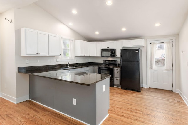 kitchen featuring a peninsula, a sink, white cabinetry, black appliances, and dark stone countertops